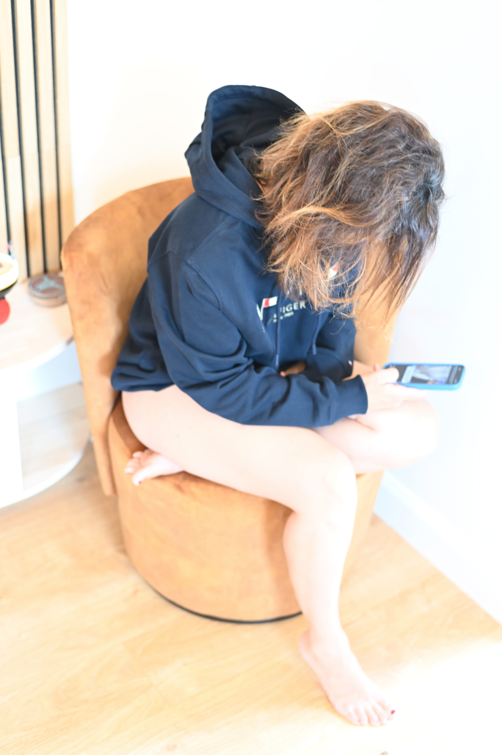Kvinne i marineblå hoodie sitter avslappet på gulvet med telefon ved siden av seg