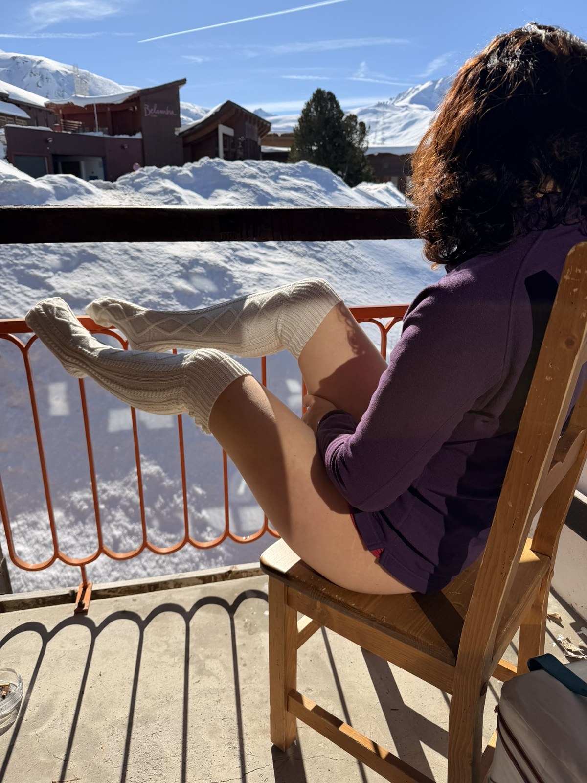 Klara sitter på en snødekt terrasse i ullsokker og strikkegenser, med snøfonner i bakgrunnen